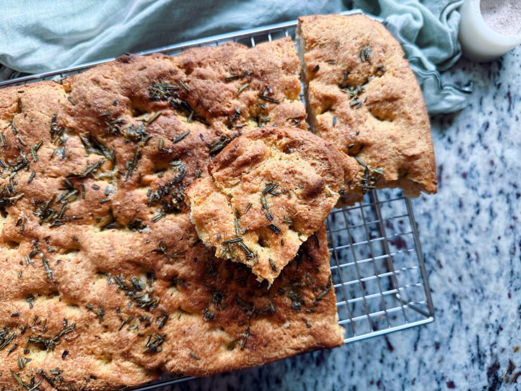 Freshly baked focaccia bread topped with herbs, resting on a cooling rack.