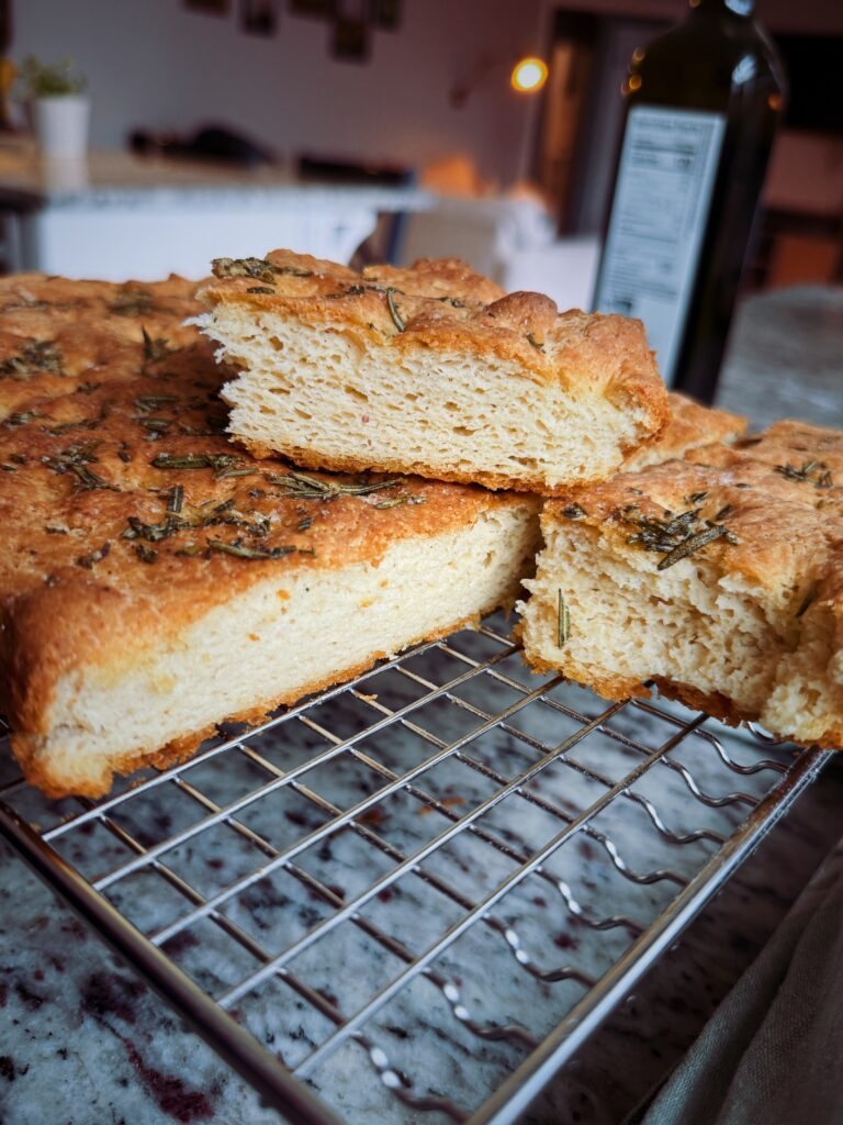Freshly baked bread with a golden crust and rosemary on top, displayed on a wire cooling rack.