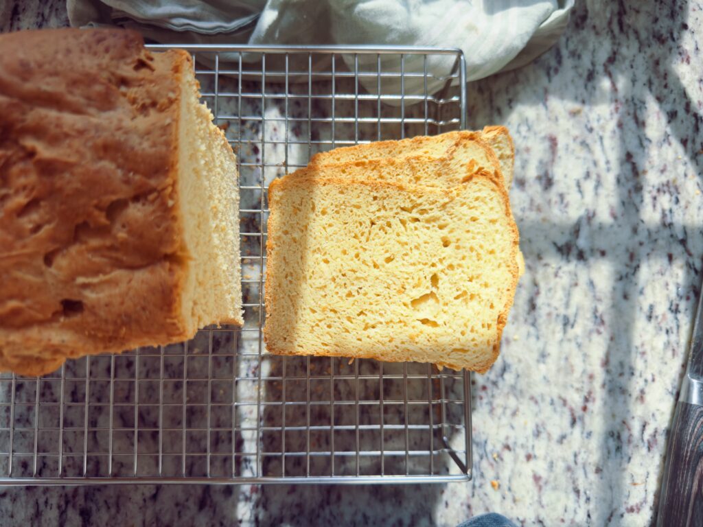 Freshly baked bread loaf on a cooling rack, with one slice cut and displayed beside it.