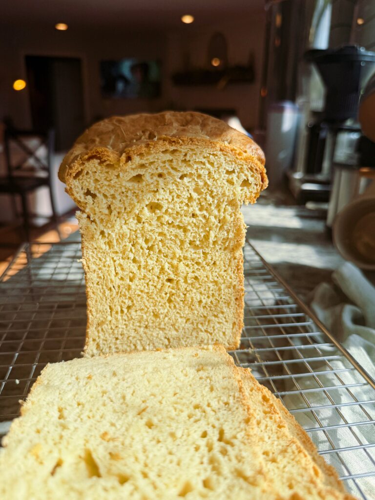 Freshly baked loaf of bread sliced on a wire rack, showcasing its airy texture and golden crust.
