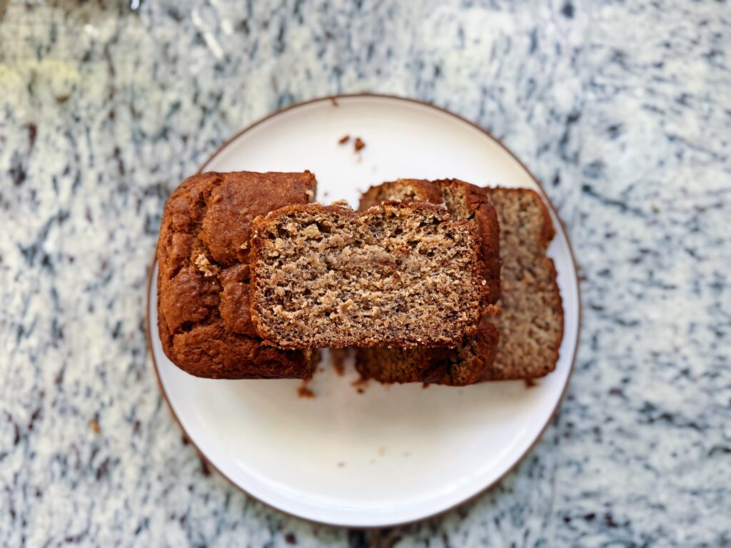 A freshly baked loaf of bread sliced on a white plate, showcasing its soft texture and golden brown crust, placed on a speckled granite countertop.