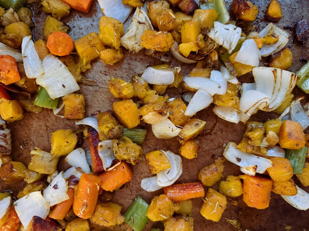 A close-up image of roasted butternut squash, carrots, celery, and onions, showcasing their caramelized edges and vibrant colors on a baking sheet.