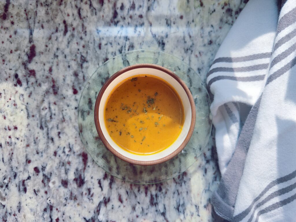 A bowl of creamy butternut squash soup topped with herbs, resting on a granite countertop next to a striped kitchen towel.