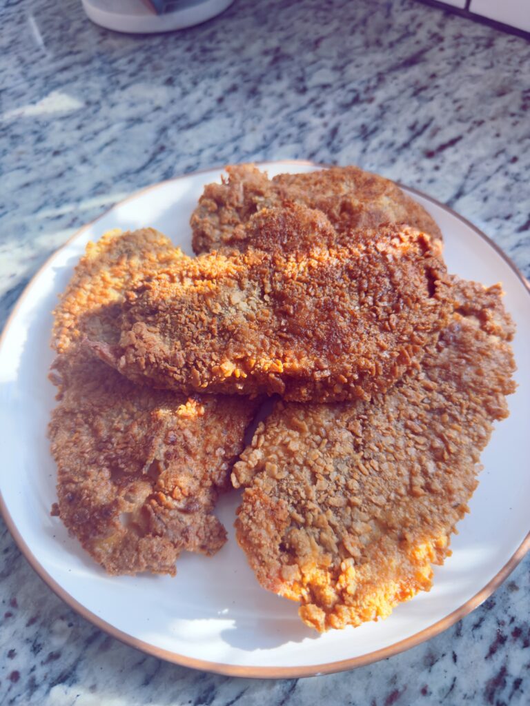 A plate of crispy gluten-free chicken schnitzel cutlets, golden brown and served on a marble countertop.