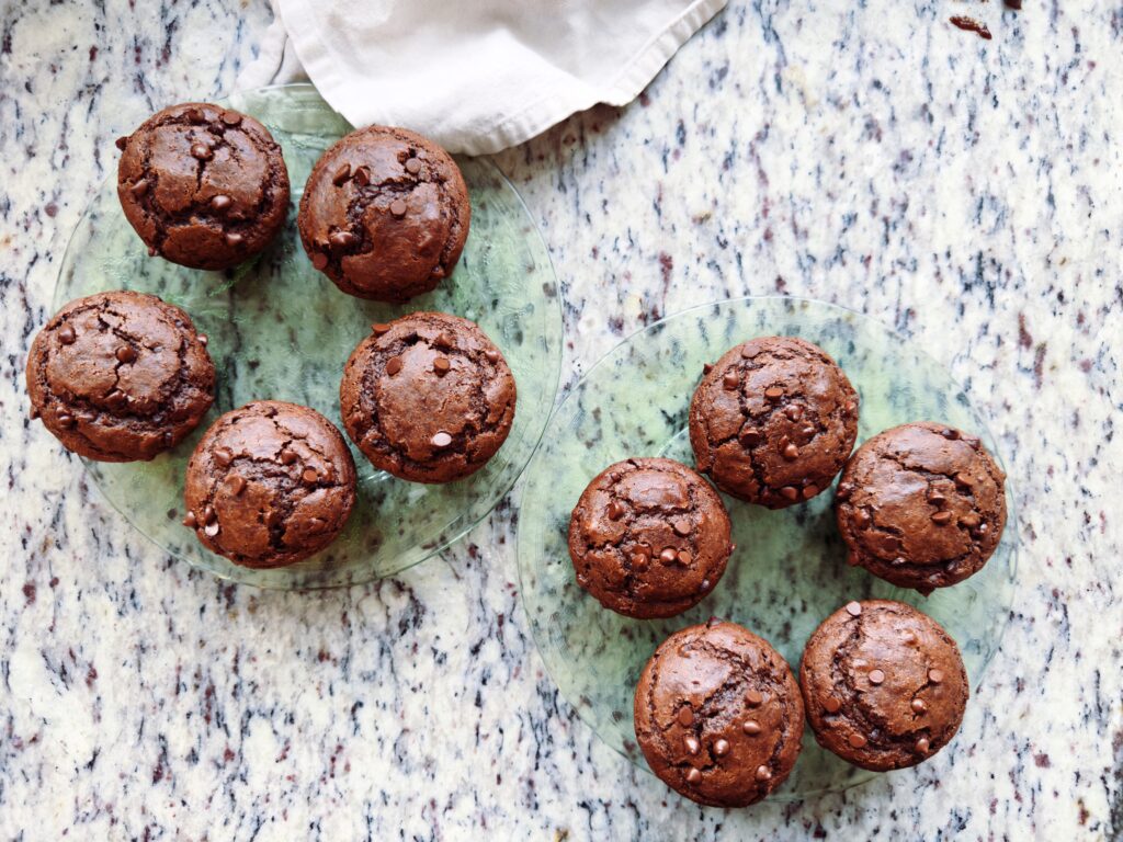 A close-up of chocolate muffins arranged on a glass plate, set on a speckled countertop.