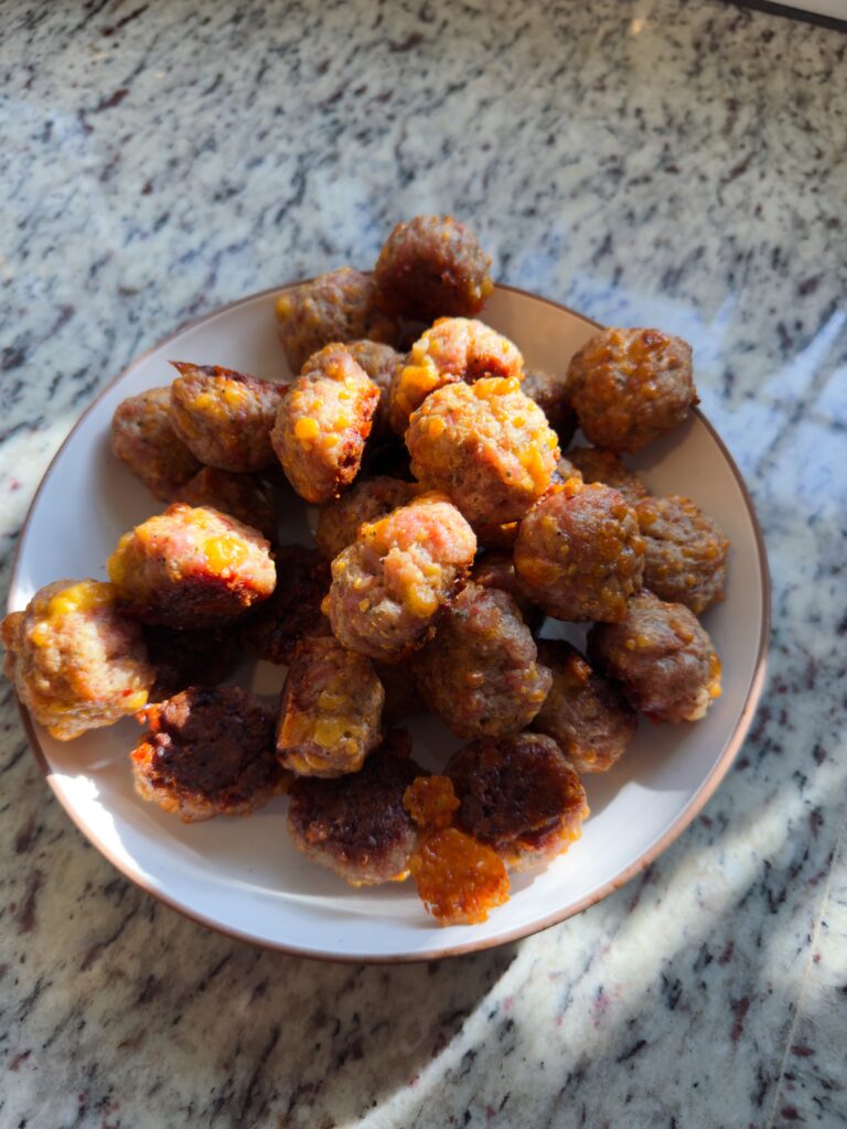 A plate of homemade gluten-free sausage balls, golden and crispy, arranged neatly on a white dish atop a granite countertop.