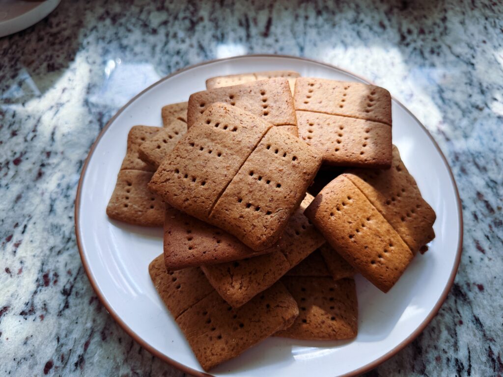 A plate of assorted brown and beige rectangular cookies stacked neatly on a marble countertop, with sunlight casting soft shadows.