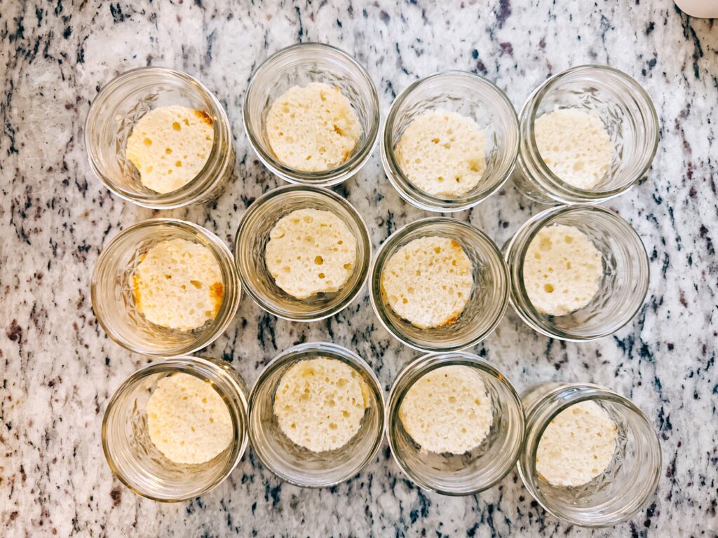 Twelve glass jars filled with sponge cake pieces on a marble countertop.