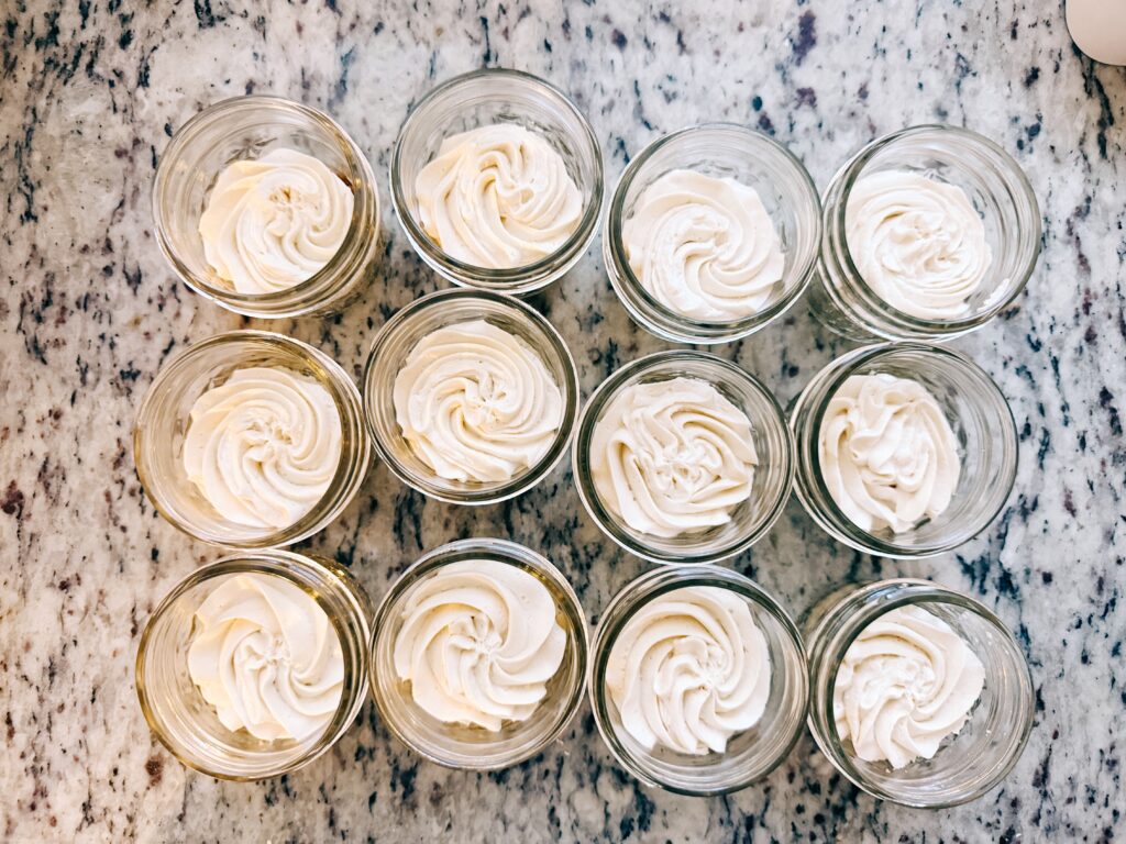 Twelve glass jars filled with creamy whipped topping arranged in a grid on a marble countertop.