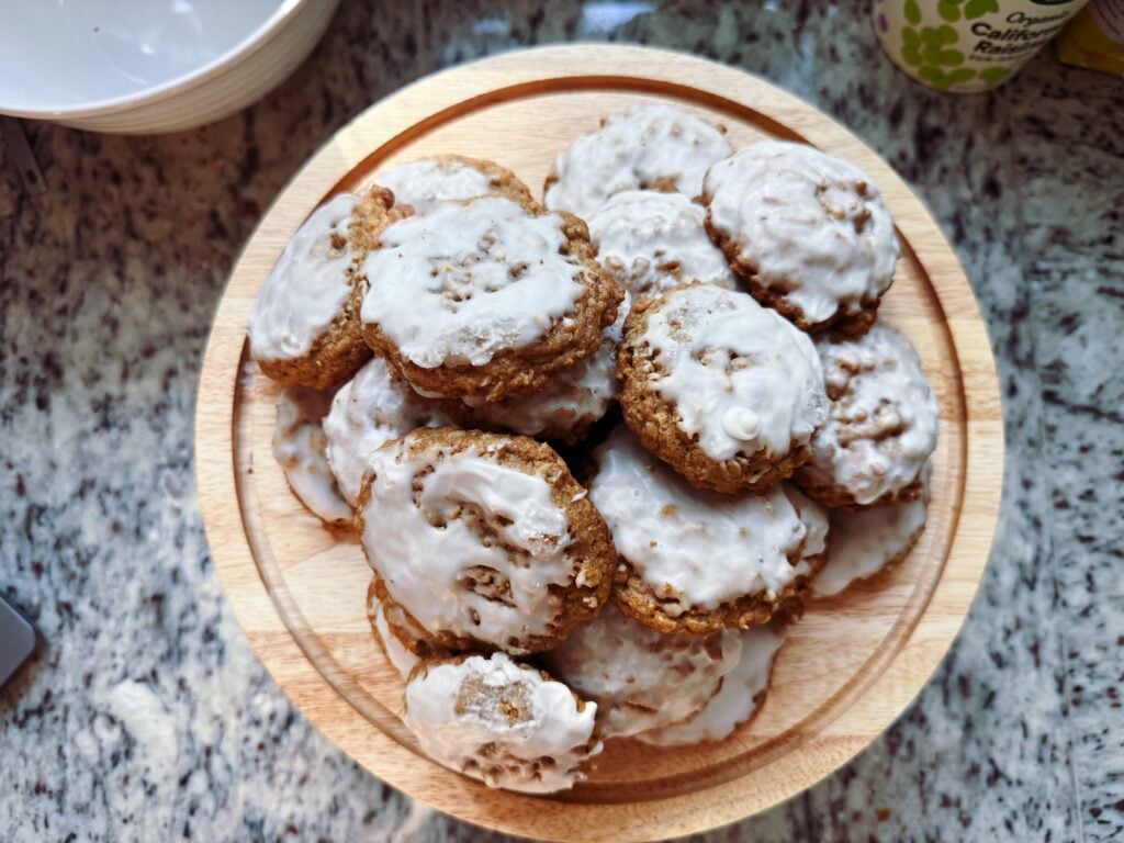A wooden plate filled with baked cookies topped with white icing, placed on a granite countertop.