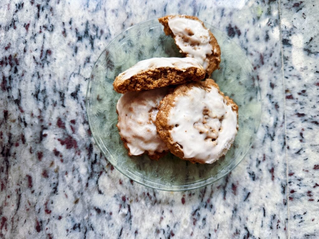A glass plate with three iced cookies, one partially eaten, placed on a speckled granite countertop.