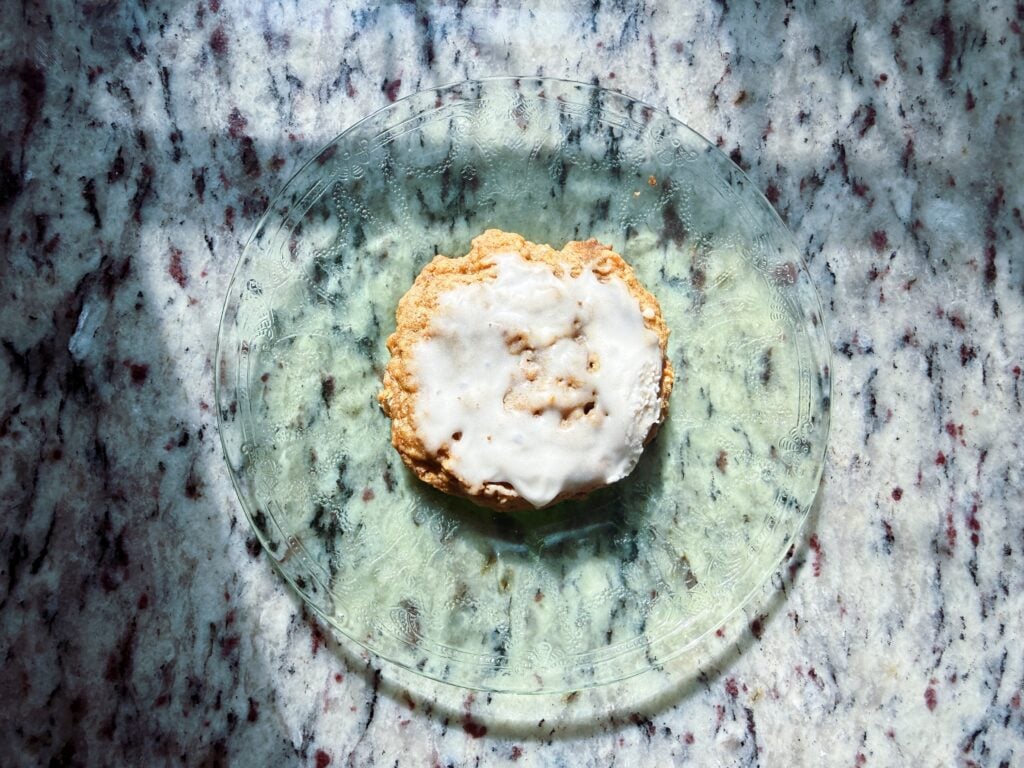 A freshly baked cookie with white icing on a glass plate, set against a speckled marble countertop.